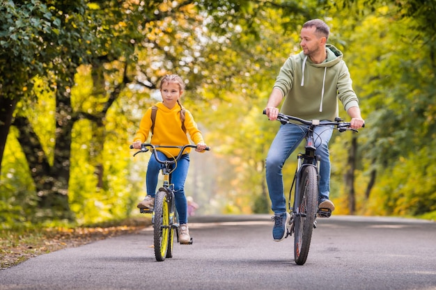 Felice padre e figlia vanno in bicicletta nel parco autunnale in una giornata di sole