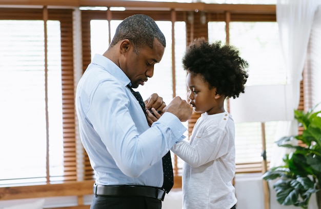 Felice padre e figlio afroamericano trascorrono del tempo insieme Ragazzino che aiuta suo padre a legare la cravatta a casa