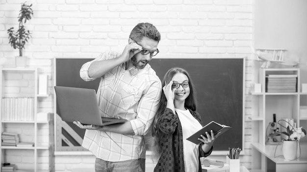 Felice padre e figlio studiano a scuola con libro e computer portatile su sfondo lavagna