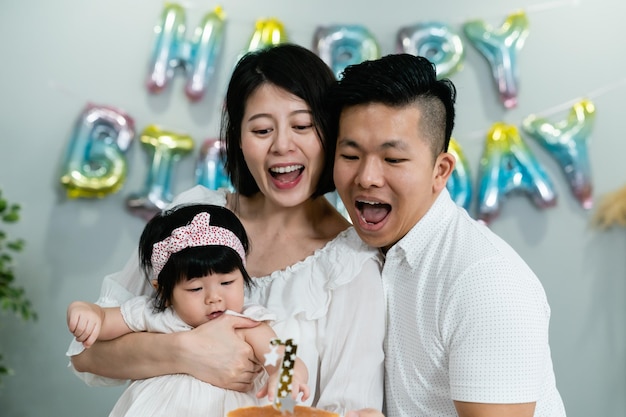 felice papà e mamma asiatici guardando la deliziosa torta di compleanno per la loro bambina di un anno alla festa di celebrazione a casa