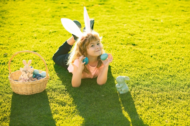 Felice Pasqua Bambino ragazzo in costume da coniglio con orecchie da coniglio a caccia di uova di Pasqua sull'erba nel parco primaverile