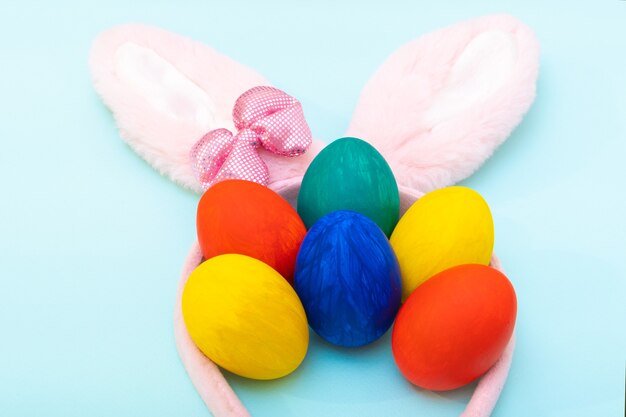 Felice Pasqua concetto. Uova di Pasqua dipinte a mano e orecchie di coniglietto rosa su una superficie blu, primo piano. Carta di Pasqua minimalista