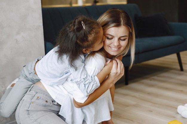 Felice piccola ragazza afroamericana che si arrampica sulle spalle della madre bionda sorridente. Madre e figlia che si abbracciano.