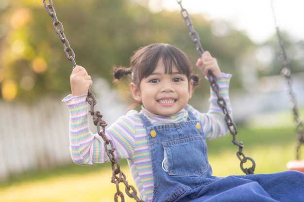 Felice piccola ragazza asiatica che gioca a swing all'aperto nel parco