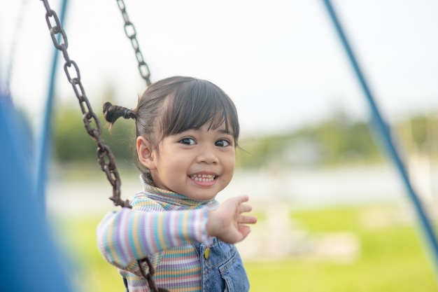 Felice piccola ragazza asiatica che gioca a swing all'aperto nel parco