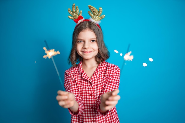 Felice piccola ragazza che guarda con ammirazione lo sparkler che brucia in mano su sfondo blu