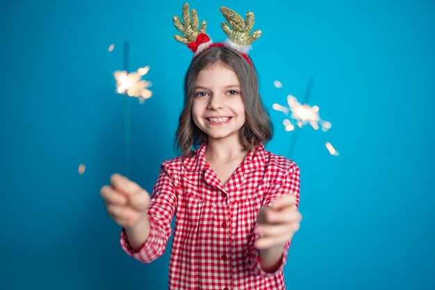 Felice piccola ragazza che guarda con ammirazione lo sparkler che brucia in mano su sfondo blu