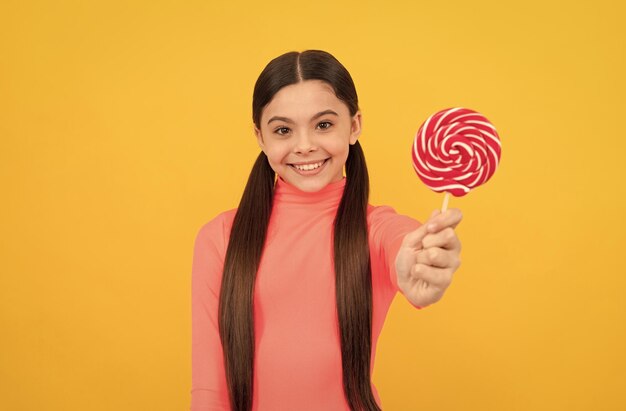 Felice ragazza adolescente con caramelle lecca-lecca sul bastone su sfondo giallo negozio di caramelle