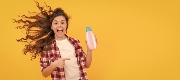 Felice ragazza adolescente con lunghi capelli ricci tenere bottiglia di shampoo divertente Banner di bambino ragazza capelli cura studio poster intestazione con spazio per la copia