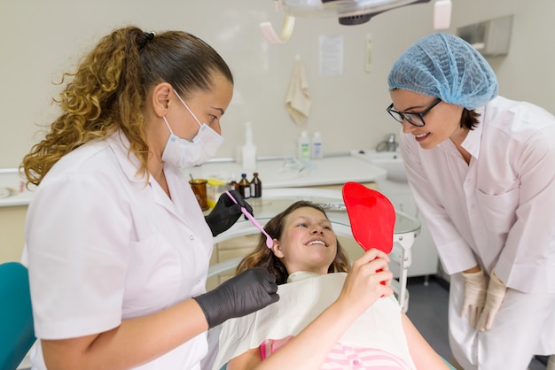 Felice ragazza adolescente paziente guardando nello specchio atteeth, seduto nella poltrona del dentista