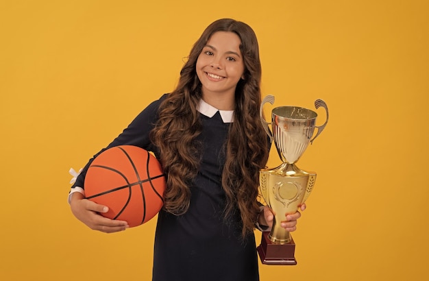 Felice ragazza adolescente tenere palla da basket e coppa campione su sfondo giallo campione