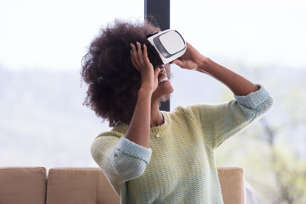 Felice ragazza afroamericana che fa esperienza usando gli occhiali VR della realtà virtuale a casa