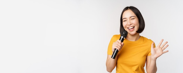 Felice ragazza asiatica ballare e cantare karaoke tenendo il microfono in mano divertendosi in piedi sopra whi