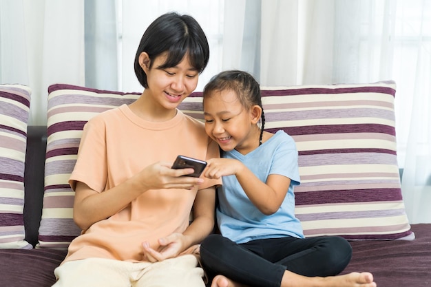 Felice ragazza asiatica con la sorella gioca insieme allo smartphone a casa