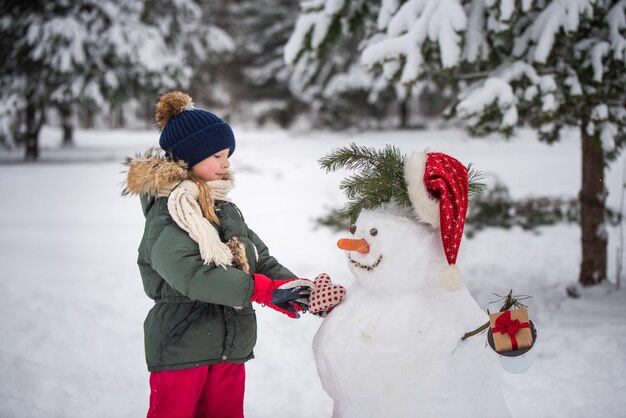 Felice ragazza bionda carina che gioca con un pupazzo di neve