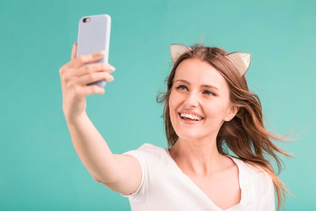 Felice ragazza bionda sorridente fa selfie tramite smartphone su sfondo blu