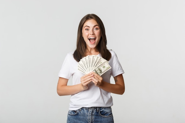 Felice ragazza bruna attraente che tiene soldi e sorridente eccitato, bianco.