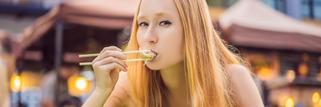 Felice ragazza carina che mangia cibo di strada e sembra divertente in un tradizionale piccolo striscione da fiera lungo