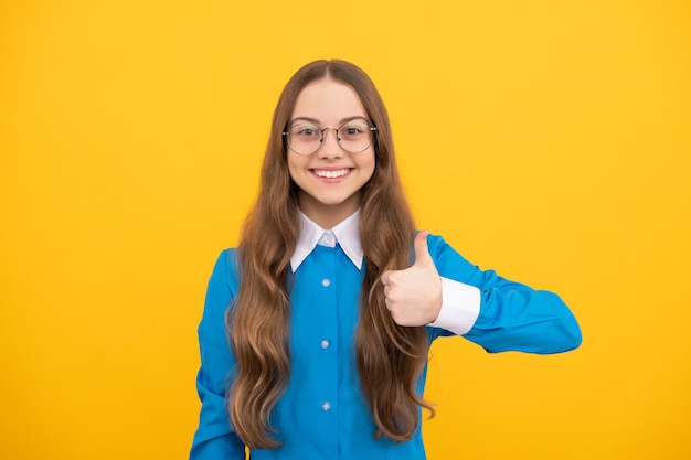 Felice ragazza dall'aspetto nerd dà i pollici in su soddisfazione gesto della mano sfondo giallo infanzia