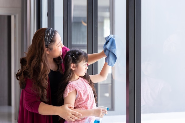 Felice ragazza figlia con mamma madre pulisce e lava insieme il vetro della finestra come buon lavoro di squadra per l'attività di pulizia durante il fine settimana a casa