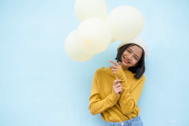 Felice ragazza giovane tenere palloncini gialli su sfondo blu.