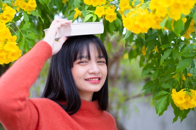 Felice ragazza indossare maglione arancione tenere il libro su sfondo giallo fiore.