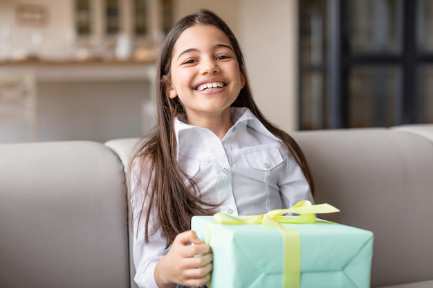 Felice ragazza mediorientale con confezione regalo seduto a casa