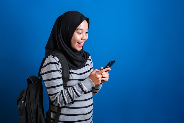 felice ragazza musulmana asiatica che macina mentre naviga in internet o legge un messaggio di chat sul suo telefono