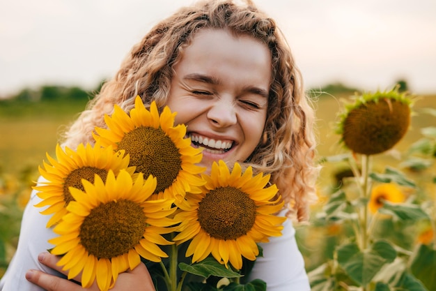 Felice ragazza riccia che abbraccia i fiori di girasole in un campo di girasoli al tramonto Ritratto di bellezza Paesaggio estivo naturale L'agronomo e l'agricoltore ispezionano la resa potenziale