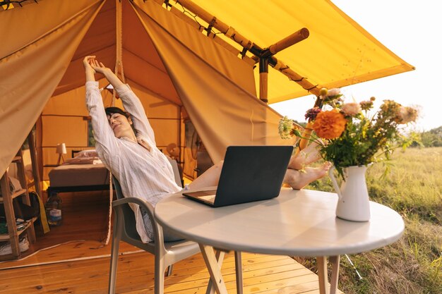 Felice ragazza rilassante in vacanza Camping giovane donna seduta in tenda da campo Giovane modello caucasico femminile leggendo il testo e lavora su notebook