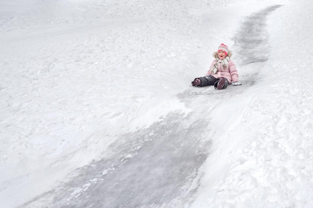 Felice ragazza sdentata in abiti caldi discende da una collina ghiacciata in un parco invernale all'aperto