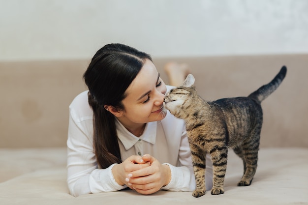 Felice ragazza sdraiata sul divano nel soggiorno vicino al gatto a strisce.