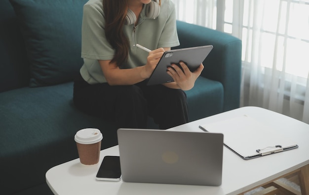 Felice ragazza teenager asiatica che tiene il pad computer gadget utilizzando la tecnologia tablet digitale seduto sul divano di casa Sorridente giovane donna che utilizza app shopping online leggendo notizie navigando in internet sul divano