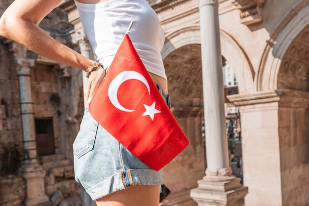 Felice ragazza viaggiatrice con la bandiera turca in mano e la famosa porta o l'arco di Adriano ad Antalya Festa nazionale e imperdibile per visitare i siti turistici e turistici in Turchia