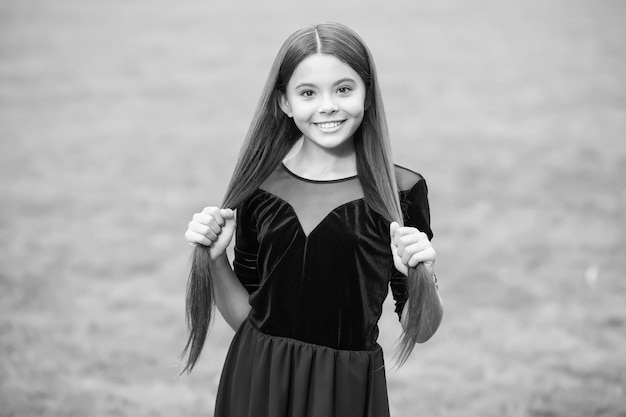 Felice ragazzina con bellezza sguardo sorriso tenendo lunghi capelli bruni in moda vestito erba verde estate soleggiato all'aperto salone