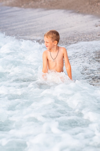 Felice ragazzino attivo che si diverte tra le onde al mare