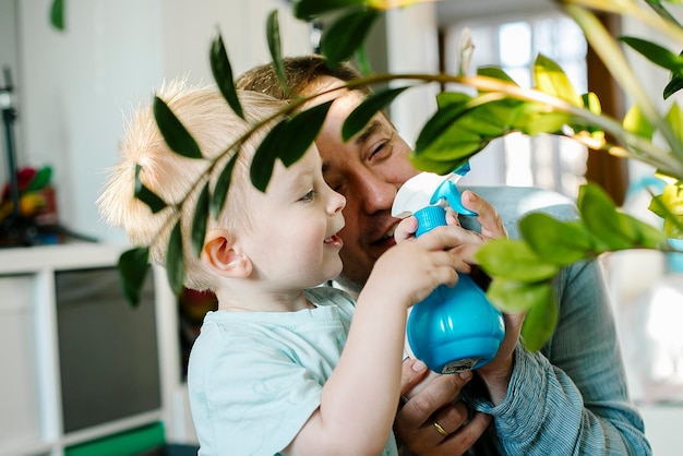 Felice ragazzino e uomo spruzzano acqua su un fiore di casa Padre papà e figlio del bambino divertendosi