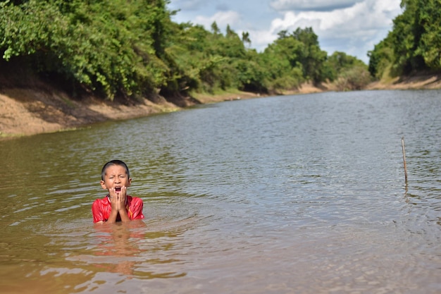 Felice ragazzo asiatico che gioca con l'acqua nel fiume