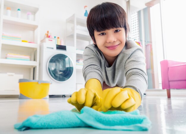 Felice ragazzo asiatico con guanti di gomma sta pulendo il pavimento, aiutando la famiglia nelle faccende domestiche.