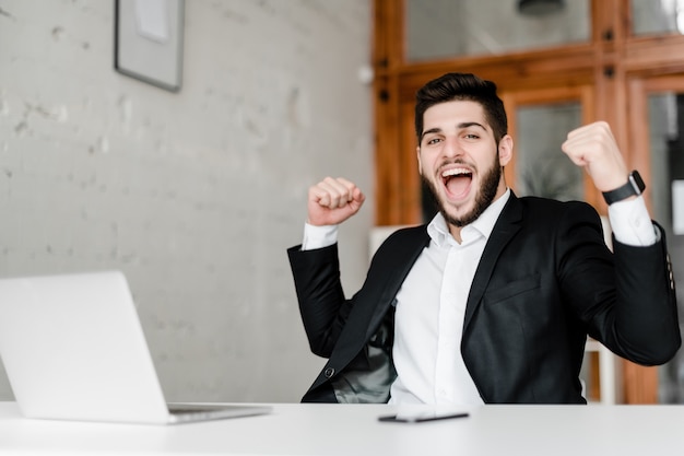 Felice ragazzo attraente sul posto di lavoro con il portatile in ufficio