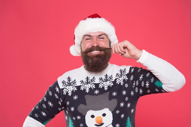 Felice ragazzo barbuto in caldo maglione lavorato a maglia e cappello di babbo natale celebra le vacanze invernali di natale e si sente allegro per i regali di natale, la cura dei capelli in inverno.