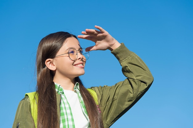 Felice ragazzo carino con gli occhiali guarda avanti cielo azzurro soleggiato all'aperto, futuro.