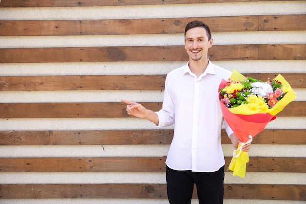 Felice ragazzo europeo in una camicia bianca e jeans neri in possesso di un grande mazzo di fiori