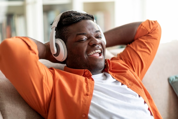 Felice ragazzo nero che ascolta il podcast utilizzando le cuffie wireless