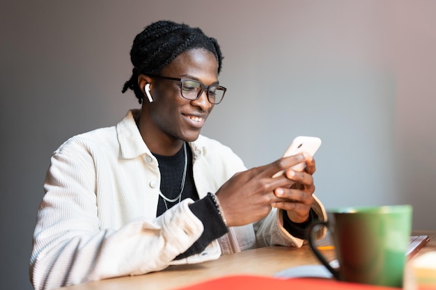 Felice ragazzo nero libero professionista che legge messaggi di testo sullo smartphone mentre lavora in remoto da casa