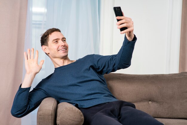 Felice ragazzo positivo, giovane uomo bello rilassato parlando, guarda il suo cellulare, smartphone