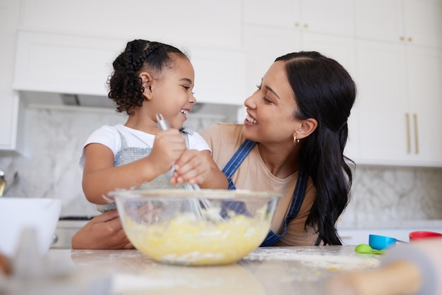 Felice razza mista madre e figlia che cuociono e si legano Giovane donna che aiuta sua figlia a cuocere a casa Madre sorridente con in mano un uovo che cucina con sua figlia Piccola felice che mescola una ciotola di pastella