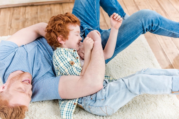 Felice rosso padre e figlio che giocano insieme sul tappeto a casa divertimento in famiglia a casa concetto