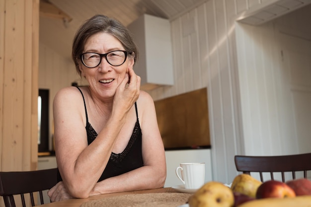 Felice senior 60s donna con gli occhiali seduto al tavolo della cucina