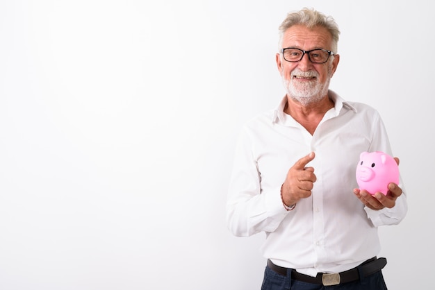 felice senior uomo barbuto sorridente mentre si tiene il salvadanaio e puntare il dito verso l'alto con gli occhiali su bianco